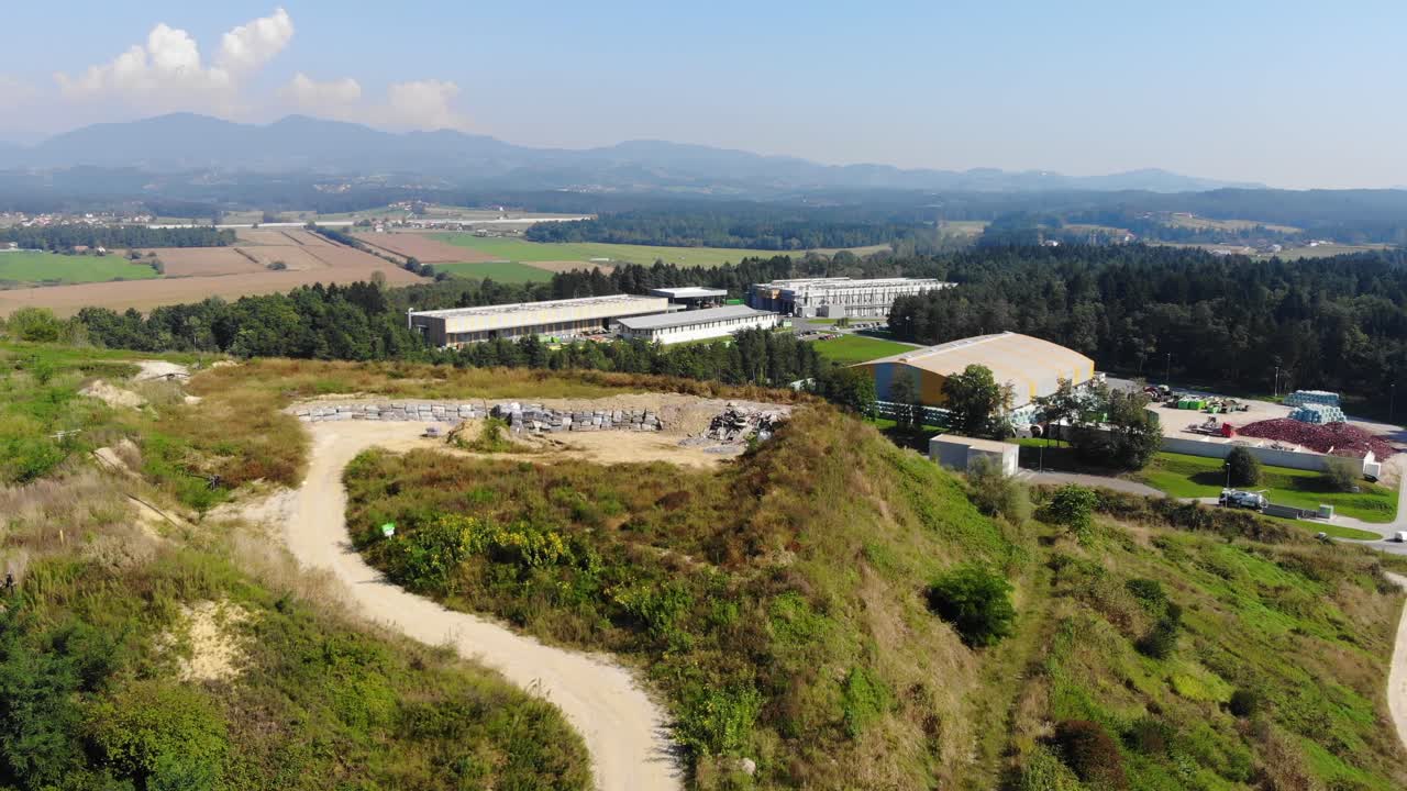 A Hill used to store materials for industrial waste site construction, a plastic recycling plant is seen closeby, Aerial flyover view