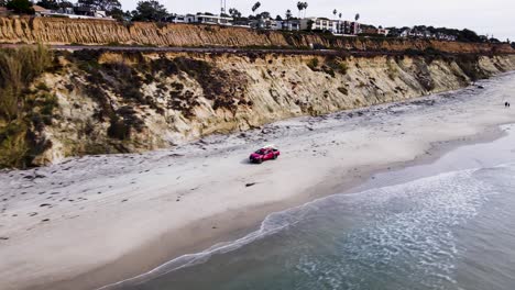 aerial view of a red lifeguard truck driving on the beach near the cliffs in delmar