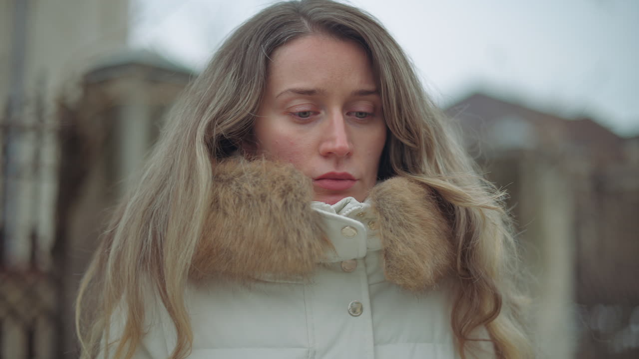 Close up of a pensive woman standing outdoors on a cold day, wearing a white winter coat with a fur collar