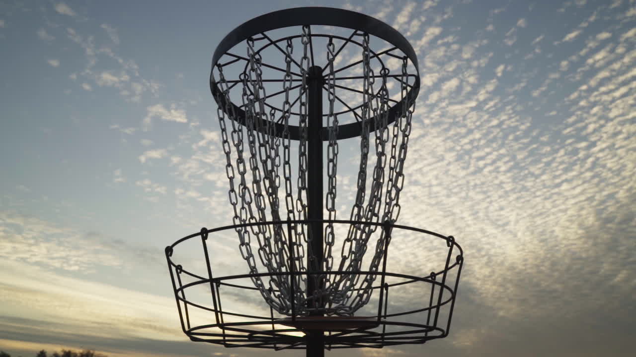 cámara lenta del frisbee de golf de disco entrando en la canasta de golf de disco y recuperada a mano por un hombre con siluetas