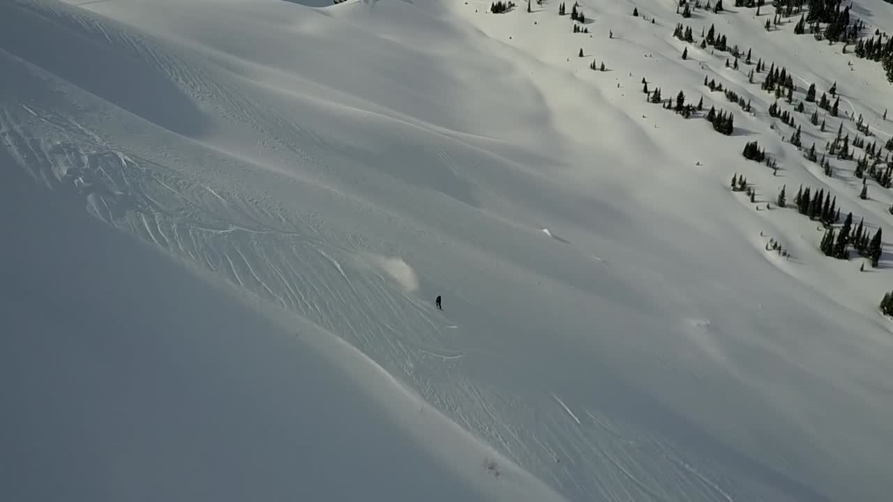 drone rastreando a un snowboarder bajando una pendiente en polvo en el interior del país