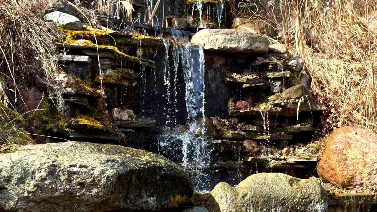 Water flows over layered rocks and moss in a natural outdoor rocky waterfall setting