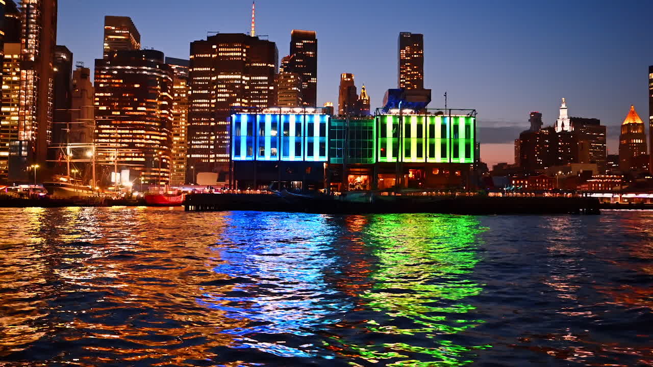 Colorful reflections on water in New York at night. Bright illuminated building with rainbow colors reflecting on the water in New York City at night