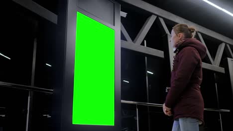 green screen concept - woman looking at blank interactive green display kiosk