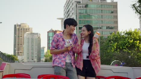 asiatic young happy couple travel together on open bus touring a modern capital city while dancing listening to pop summer hit and making soap bubble with a toy gun