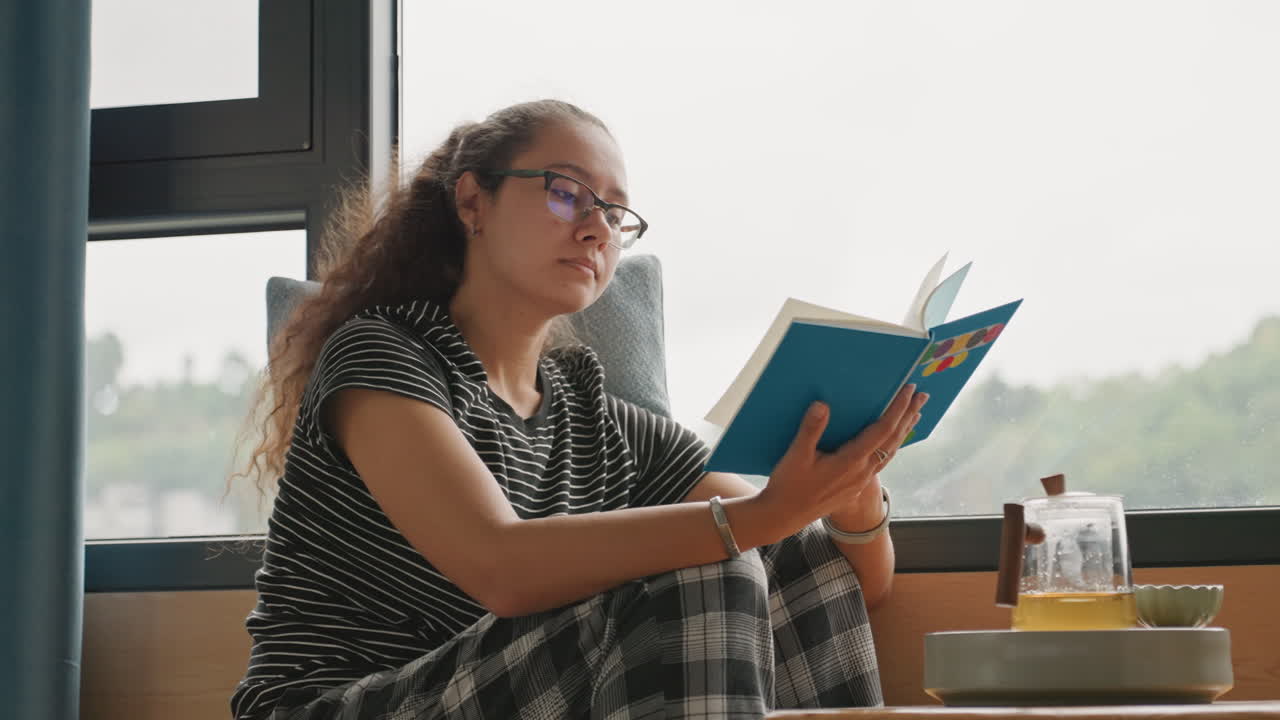 Une jeune fille contemple la vue depuis la fenêtre. Une jeune femme observe le paysage à travers la vitre. Une femme lit un journal dans une chambre d'hôtel calme. Une femme observe le paysage depuis la fenêtre de l'hôtel avec une expression contemplative.