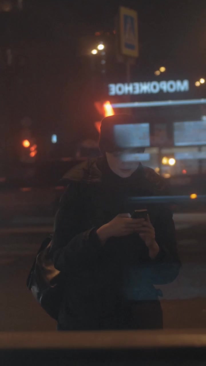 Donna con cellulare alla fermata dell'autobus in città di notte