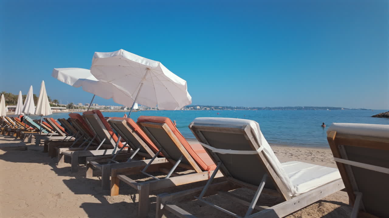 Row of empty sun loungers with white umbrellas on a sandy beach by the calm blue sea