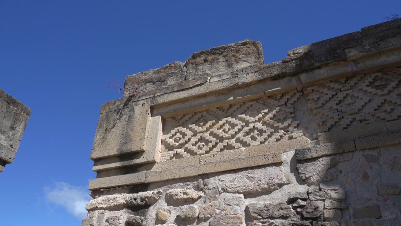 Tomada estática em ângulo baixo de um detalhe de muro de pedra zapoteca antigo com mosaico de treliça geométrica no sítio arqueológico de Mitla em Oaxaca, México.