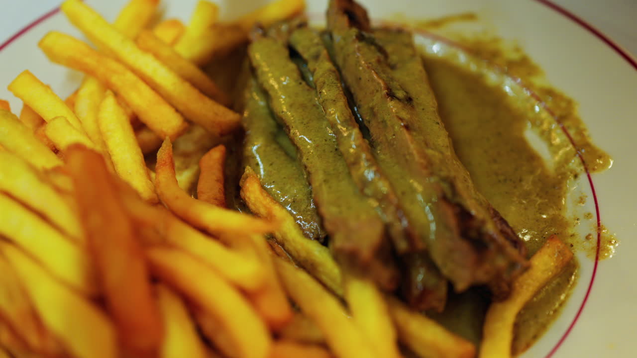 Close up of a plate of fries with meat and green sauce on a plate