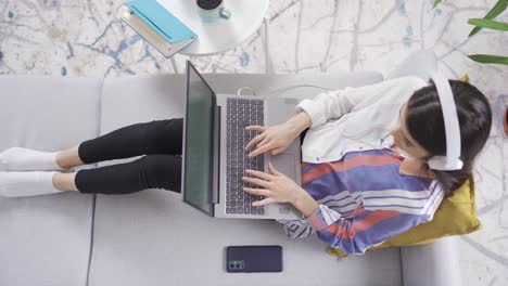 Focused-Beautiful-young-woman-using-laptop-in-living-room-at-home,-taking-notes.