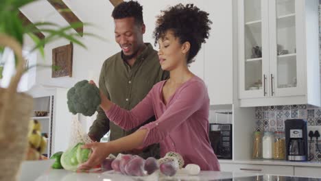 Happy-african-american-couple-with-bags-of-vegetables-in-kitchen