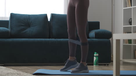 casa fitness mujer está entrenando las piernas con banda elástica deportiva tensando los músculos vista de cerca en la sala de estar entrenamiento y ejercicio