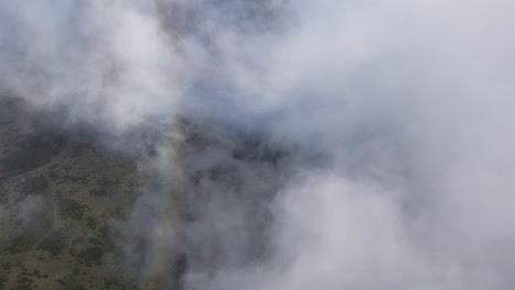 Aerial-view-of-a-colorful-rainbow-disappearing-in-white-clouds-over-the-landscape-of-Maui,-Hawaii