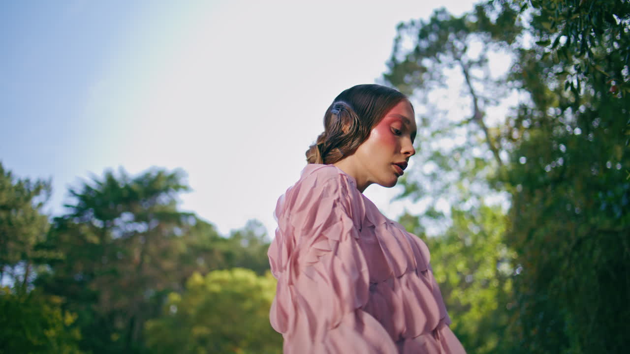 감각적인 모델이 숲의 풍경을 포즈로 하고 공기 있는 드레스를 입고 손을 움직이고 있습니다.