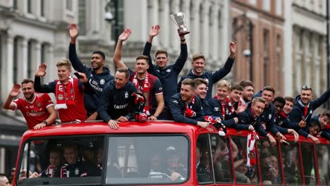 celebratory parade of triumph: a group of athletes wave enthusiastically from a vintage bus while displaying their hard-earned trophy in a joyful atmosphere