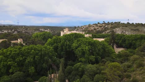 Chateau-Comtal-Provence-France,-nestled-behind-lush-green-trees,-bird's-eye-view-aerial