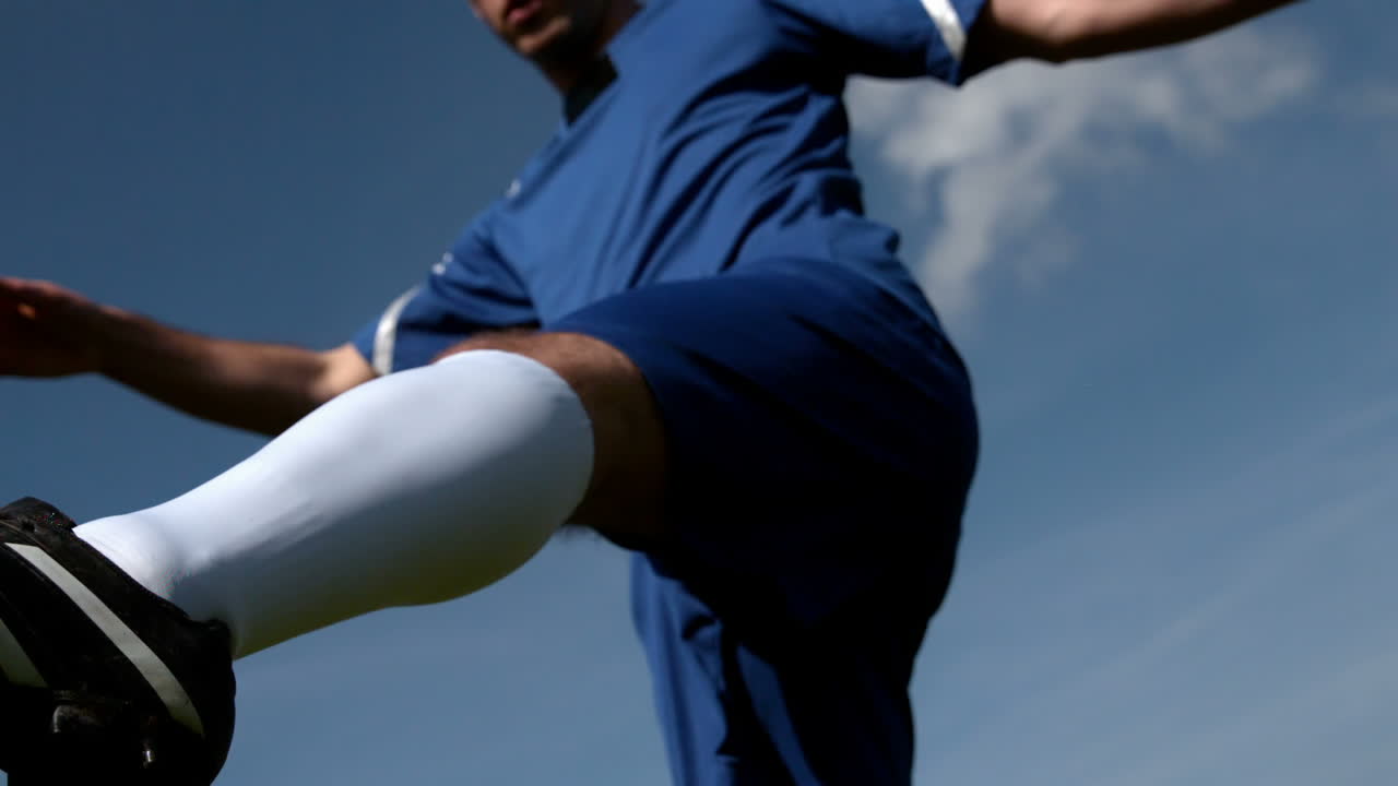 Football player kicking the ball under blue sky