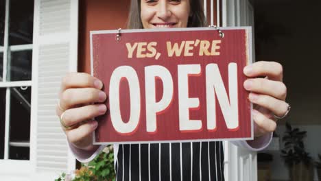 Close-up-of-smiling-caucasian-waitress-wearing-apron,-holding-open-sign