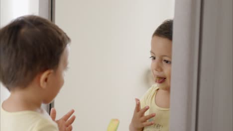 pequeño niño latino mirándose en el espejo comiendo una piruleta mirando su lengua