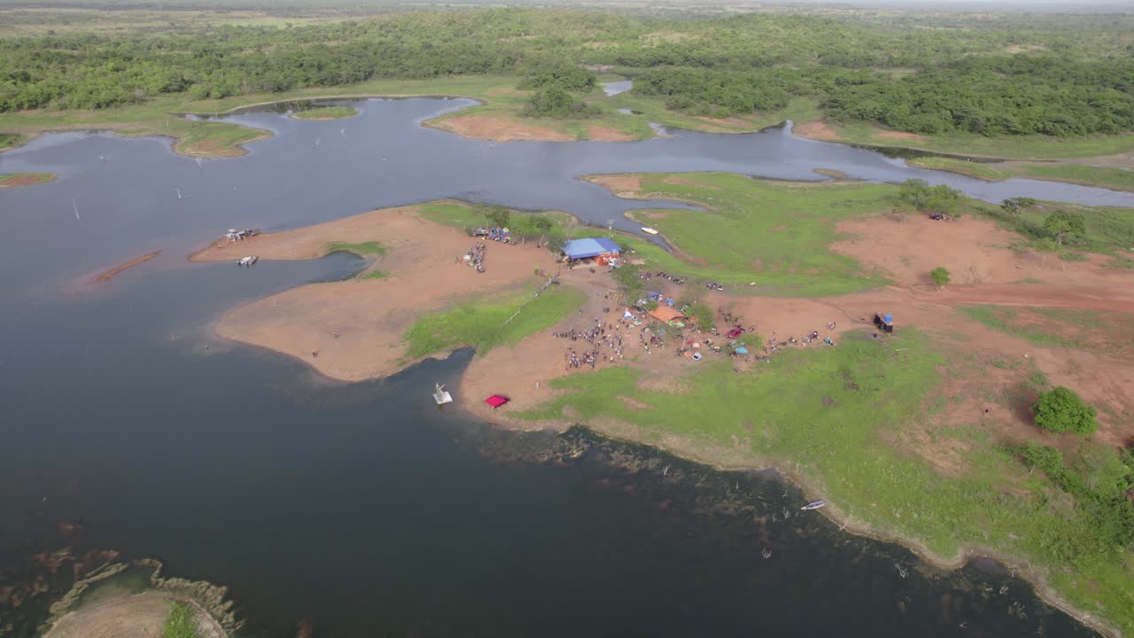 A stunning drone shot captures a lively group of campers and friends gathering on the remote shores of a tranquil lake, surrounded by untouched nature