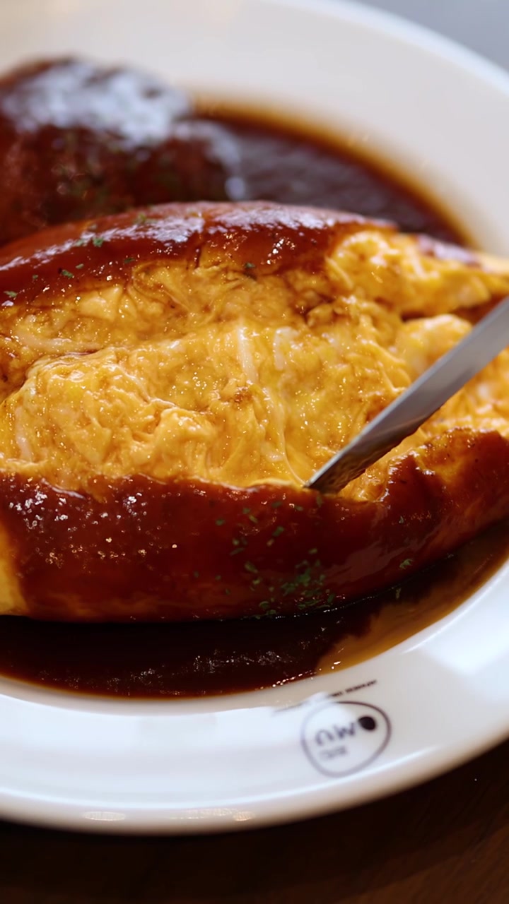 Un coltello affetta una soffice omelette giapponese sopra il riso, rivelando una consistenza morbida, una ricca demi-glace, con illuminazione naturale