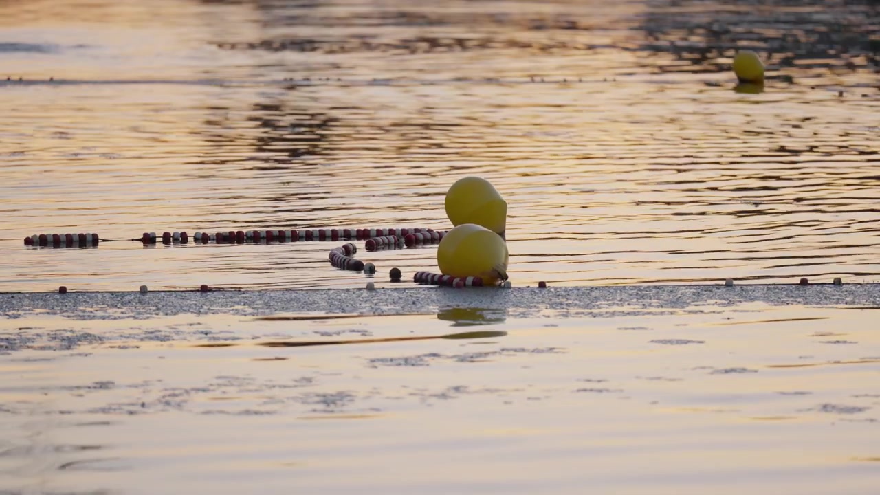 Yellow balloons and lane markers float on calm river water at sunset in Montrichard