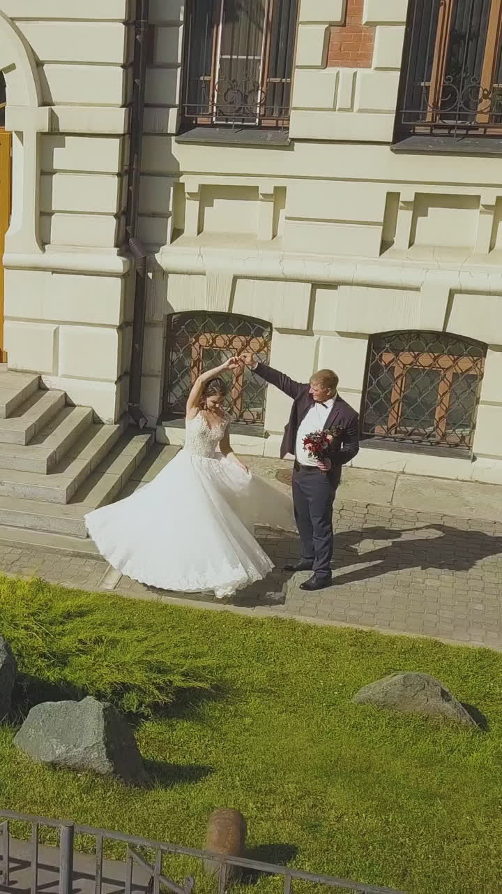 beautiful newly wedded couple dances near modern building with stylish facade at entrance steps on sunny day upper view