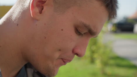 close up of white boy licking sweet with head tilted downward in quiet outdoor environment with natural daylight illuminating his face and soft focus background of green lawn and walkway
