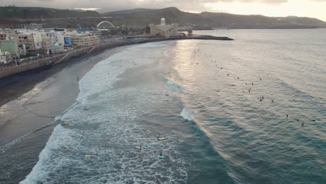 Cinematic-aerial-shot-of-surfers-at-sunset-in-the-waters-of-Las-Canteras-Beach-at-Las-Palmas-de-Gran-Canaria,-Drone