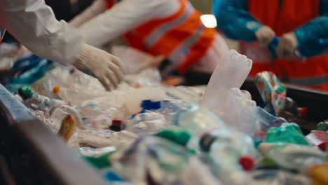 Close-up-shot-of-the-hands-of-workers-who-sort-plastic-bottles-and-garbage-near-a-conveyor-belt-at-a-waste-and-plastic-recycling-plant