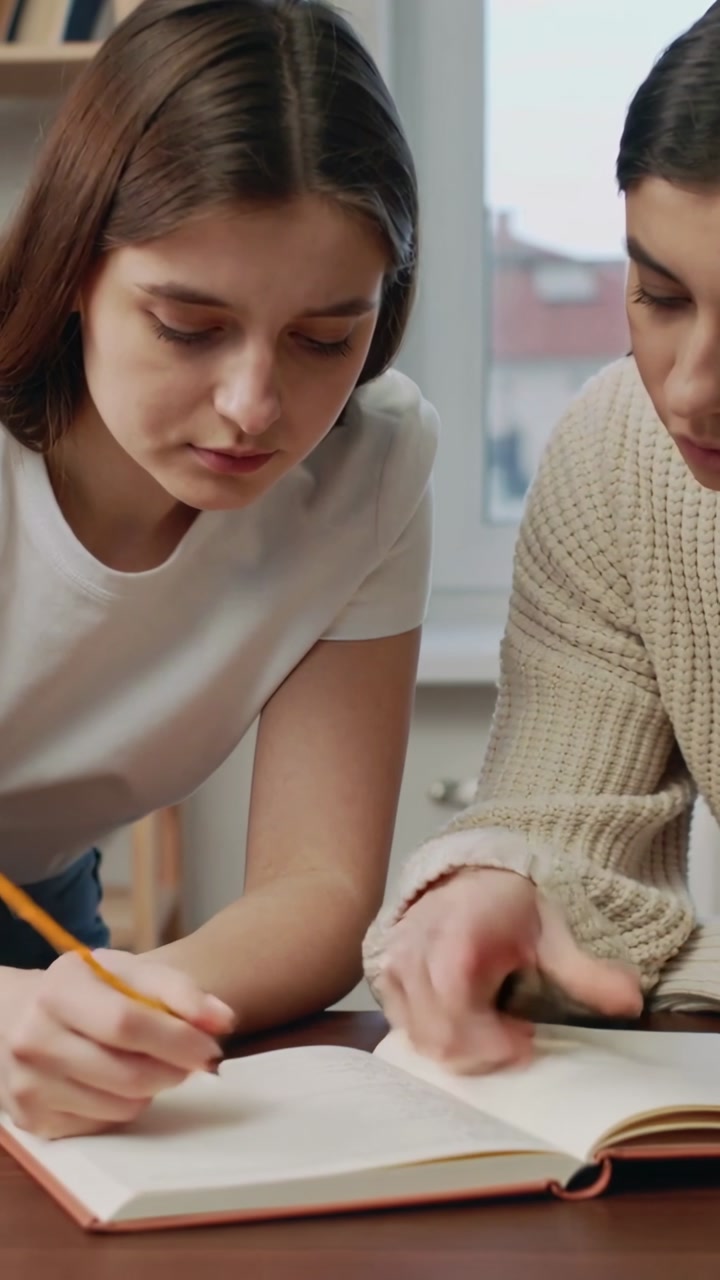 Vertical video: Pointing right sweater guiding left writing at table solving notebook yellow pencil