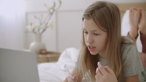 funny preteen girl is talking by video calling on laptop staying home and learning online
