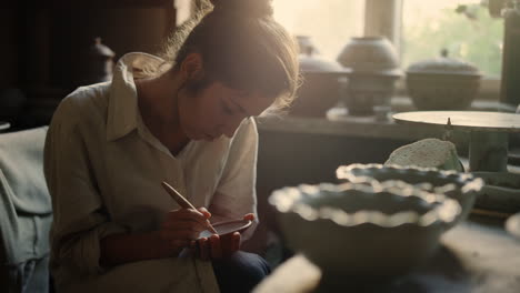 Beautiful-woman-making-ornament-on-product-in-pottery.-Girl-drawing-on-wet-clay