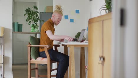 hombre albino afroamericano con rastas trabajando, usando computadora portátil y teléfono inteligente