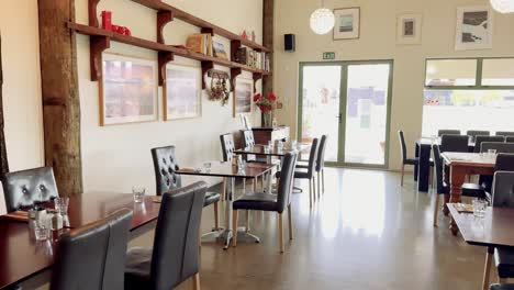 bright, contemporary cafe interior with empty tables and chairs, natural light streaming through large windows, and smooth camera pan revealing stylish dining space