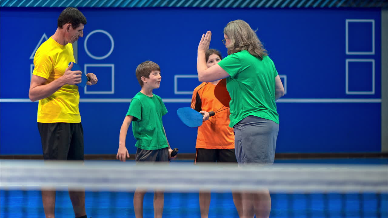 Two adults and two children high-fiving after playing pickleball on a blue, inside court