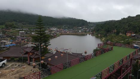 aerial drone forward moving shot over ban rak thai, chinese village near a lake in mae hong son, thailand surrounded by hilly terrain covered with fog