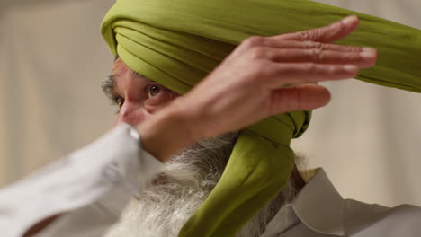 fotografía de estudio de cerca de un anciano sikh con barba atando tela para un turbante contra un fondo plano 2