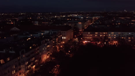 Aerial-view-of-town-at-night.-City-lights-disappearing-while-drone-descending-into-park.-Evening-traffic-in-streets-of-Berlin,-Germany.