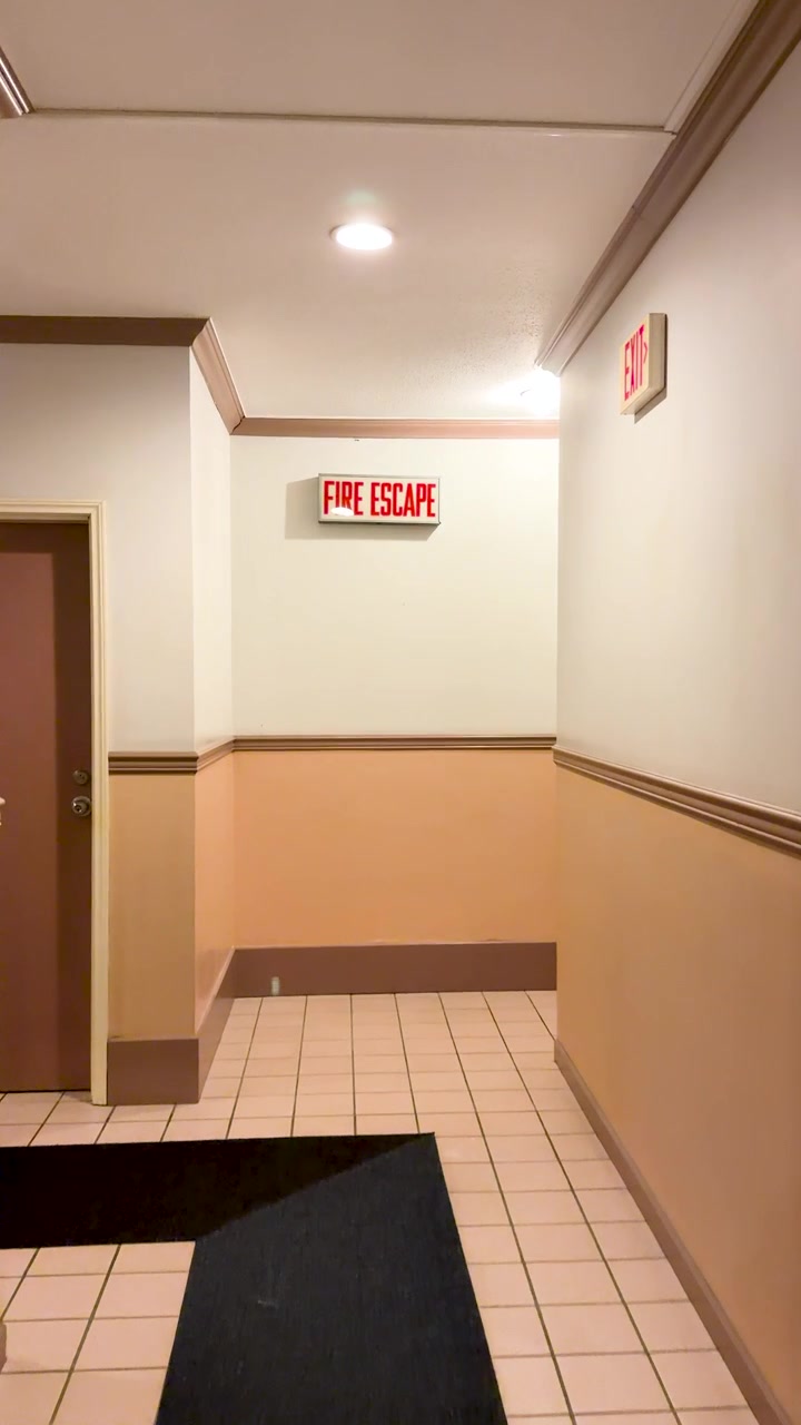 A slow camera movement through a quiet hotel corridor toward a red fire escape sign