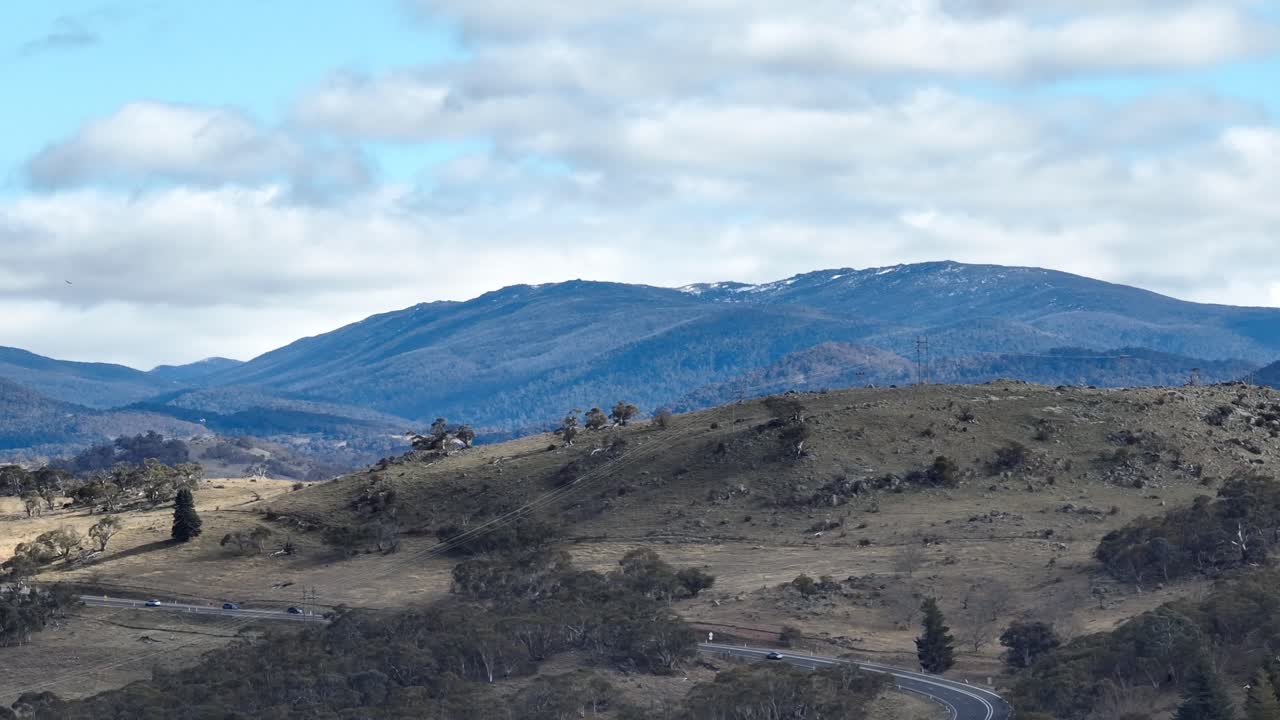 Long lens drone shot sliding past hills and snow capped mountains in the distance near Jindabyne, Australia