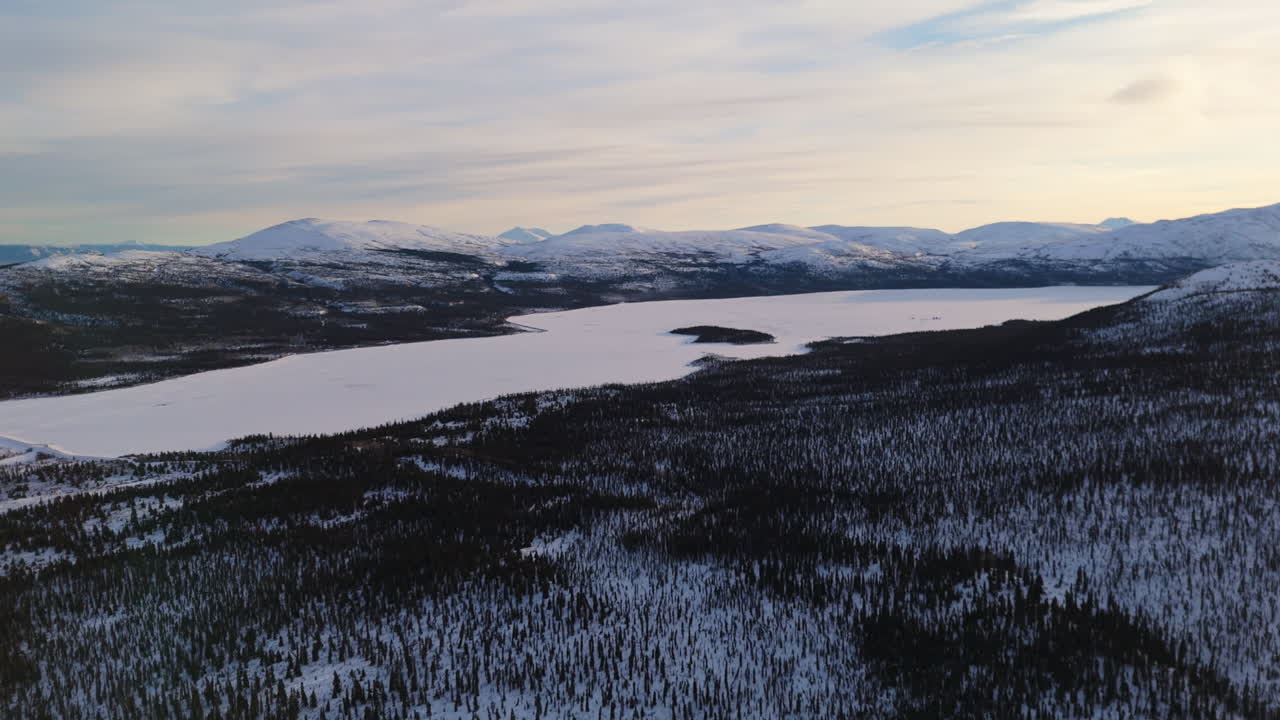 A cinematic sunset aerial shot over Fish Lake and snow-capped mountains near Whitehorse, Yukon, showcasing the untouched beauty and tranquility of Canada's northern wilderness.