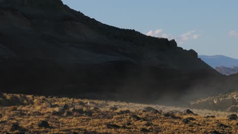 Weißes-Fahrzeug-Fährt-über-Hügel-Davon-Und-Verschwindet-An-Sonnigem-Tag-In-Staubiger-Wüstenlandschaft