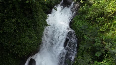 looking down on a powerful waterfall surrounded by jungle in the north of bali in the summer, aerial