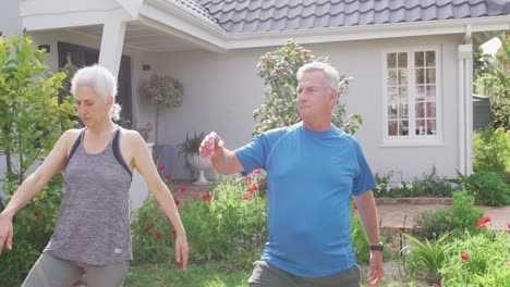 relaxed caucasian senior couple practicing yoga in front of house