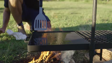 pouring oil onto an open campfire bbq in preparation for cooking