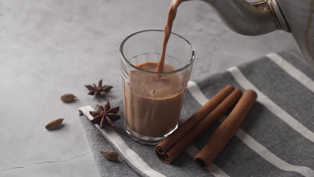 Chai indiano servito in tazze di vetro, preparato in un bollitore di metallo con masalas aromatici. Viene versato nel vetro.