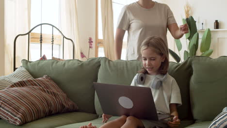 a blonde little girl doing her homework with the laptop and asking her mother to hel her with the task