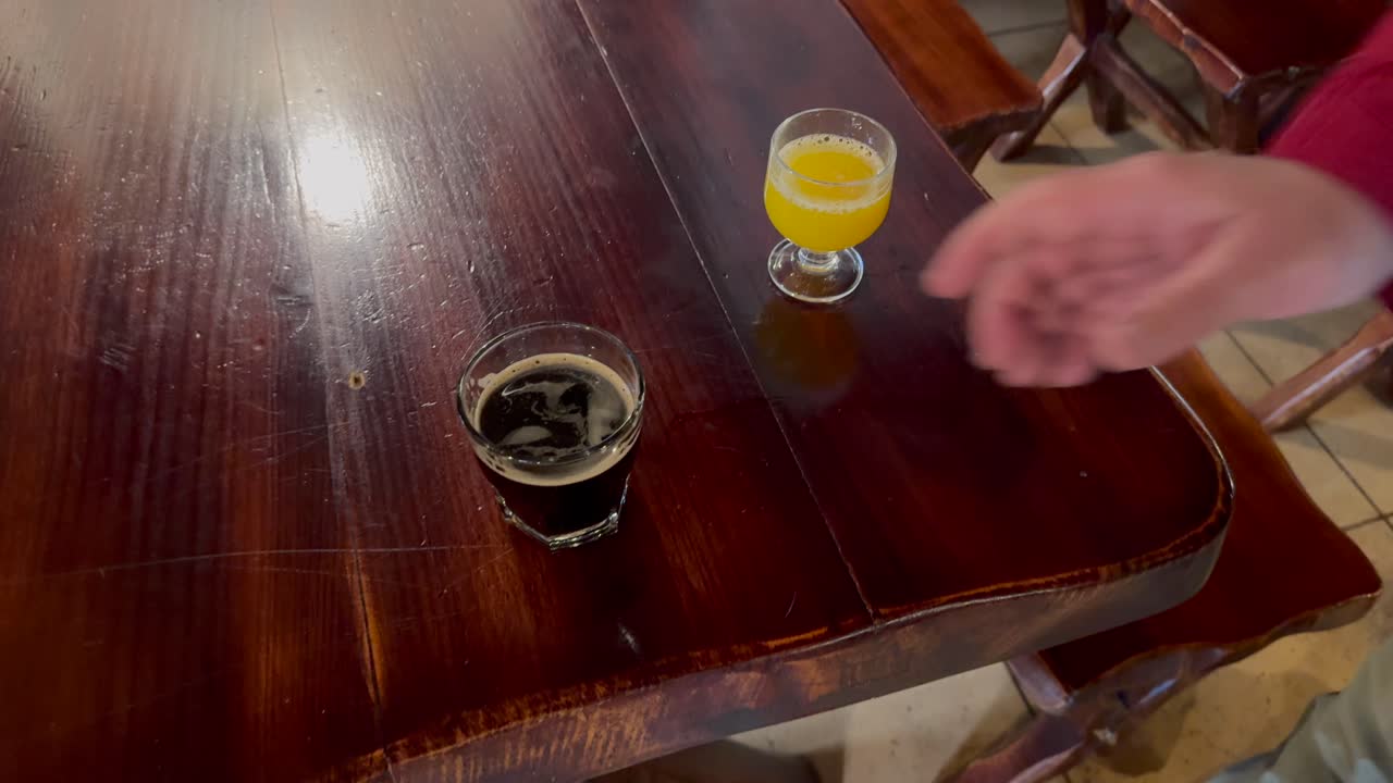 A hand picks up a soft drink glass from wooden table in a bar or restaurant